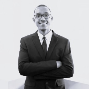 Louis Baptista, a Black man with short hair, wearing a dark suit, white shirt, and dark tie.