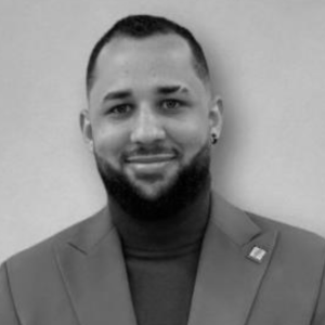 Xaviel Cruz Quiñones, a Latino man with short dark hair and a full beard, wearing a blazer.